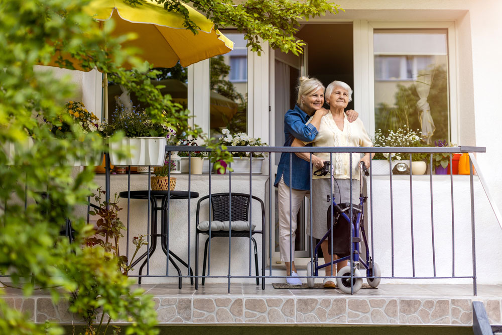 Seniorin mit Tochter auf Balkon des Pflegeheims.