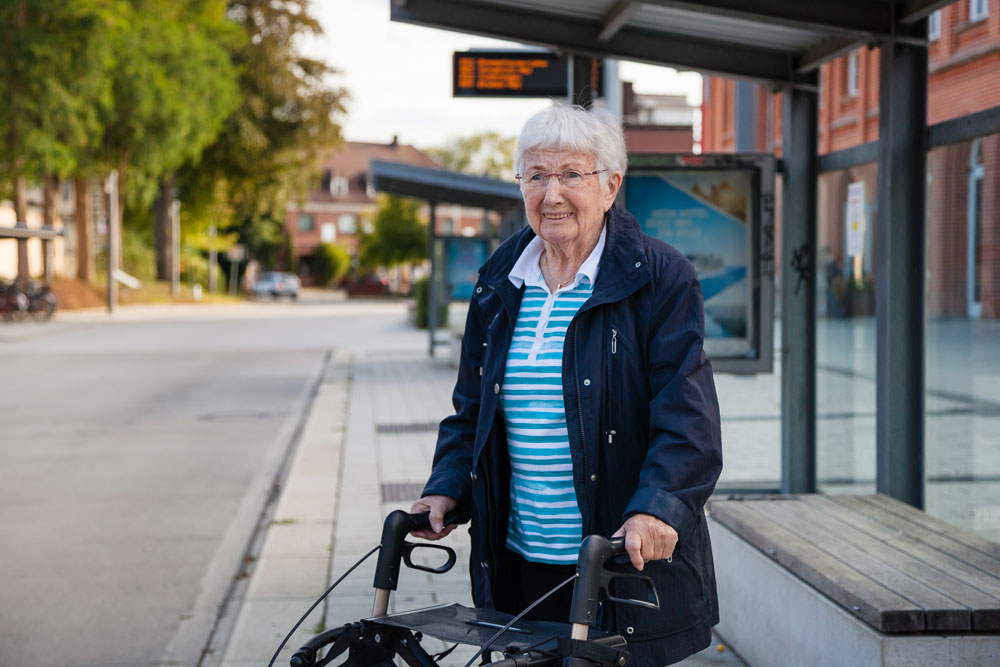 Seniorin mit Rollator wartet auf Bus.